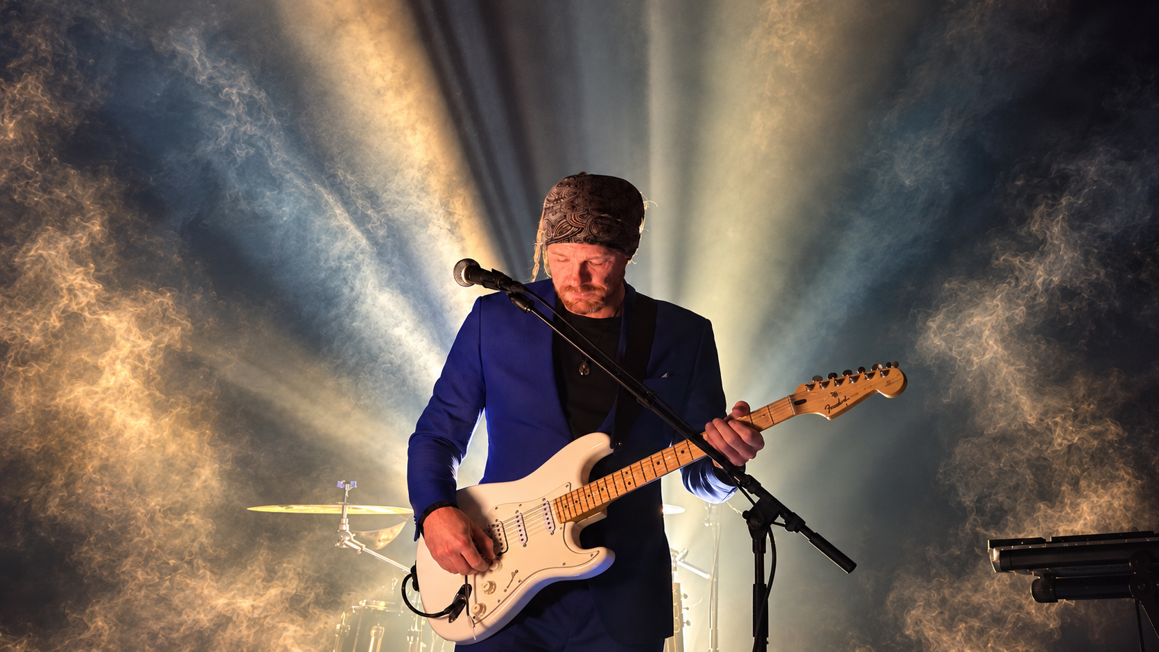 Ben Misterka playing a white Stratocaster in stage smoke and backlight